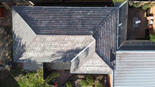 Before: roof restoration. Weathered concrete tiles restored in slate grey.